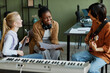 © Seventyfour - Portrait of three young musicians writing songs together, focus on black woman smiling happily and holding music sheet