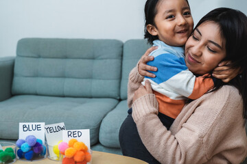 Wall Mural - Happy Latin American mother and son hugging each while playing together at home - Family love concept - Focus on mom face