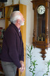 © Solid photos - Sad senior man standing at home in front of the wall clock and looking at it