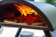 © Alex Giroux/Wirestock Creators - Closeup shot of a crusty pizza cooking in an outdoor oven in a garden