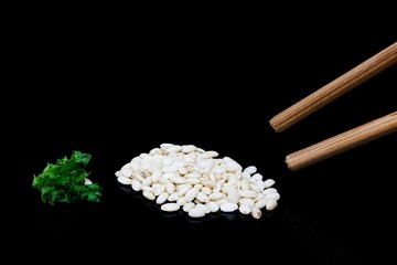 Healthy brown rice on a black reflective surface with chopsticks and green lettuce