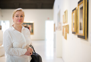 Wall Mural - Adult woman visitor enjoying at exhibition, standing near pictures in museum of arts