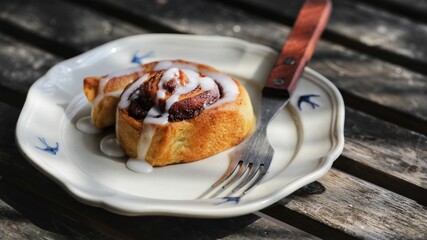 Sticker - Close-up of a delicious freshly baked cinnamon rolls on a plate next to a fork on a wooden surface