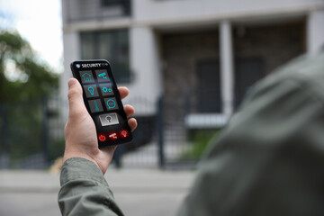 Man using home security application on smartphone in front of house outdoors, closeup