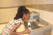 African American Kid drinking from water fountain indoors 