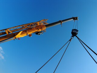 Canvas Print - Low angle shot of a yellow crane lifting heavy weights against a blue sky