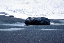 Wet Black Rock On Black Sandy Beach With Foam In The Background