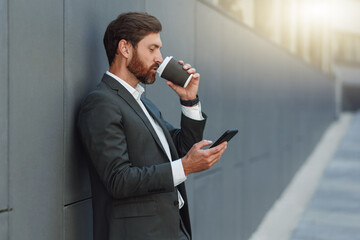 Sticker - Focused european businessman in suit with phone drinking coffee near office building during break