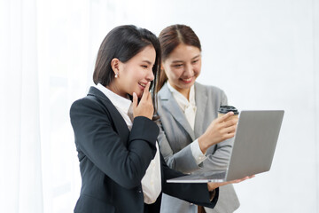 Two beautiful Asian young business women discuss work exchange idea exchange knowledge using laptop computer in the office.