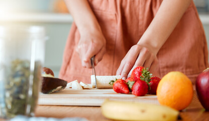 Wall Mural - Healthy woman cutting fruit to make a smoothie with nutrition for an organic diet at home. Closeup of caucasian female hands chopping fresh produce for a health drink in a kitchen.