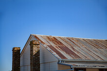 Rusty Roof And Stone Chimney Of Old Building Against Blue Sky