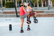 Women Do Fitness And Workout Outdoors And Jump On Trendy Kangoo Boots In The Park. Fighting Cellulite And Losing Weight