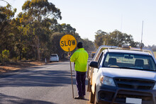 Worker Holding Slow Lollipop Sign On Edge Of Road Near Vehicle