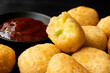 Detail of fried breaded chilli cheese nuggets next to a bowl of ketchup on dark background. One eaten.