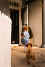 Girl Wearing Blue Dress With Brown Poodle Dog Running Towards The Front Door Of Home