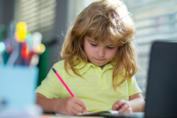 Fototapete - Serious school child writing homework in school class. Portrait of school kid boy siting on table doing homework. Child holding pencil and writing. Boy drawing on white paper at the table.