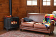 Black modern Cast iron wood stove at home. Fragment of interior of country house. Interior cozy living room with wood burning stove inside, comfortable sofa, rustic wooden walls and carpet on floor. 