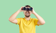 Happy Joyful Young Man In Casual Yellow T Shirt Standing Isolated On Green Background, Holding Modern Binoculars, Looking Ahead And Smiling. Making Discoveries And Having Fun While Travelling Concept