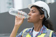 © amorn - Female engineer drinking water at construction site. African American woman engineer working at construction site on rooftop of building