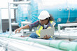 © amorn - Female engineer working with laptop computer for checks or maintenance in sewer pipes area at construction site. African American woman engineer working in sewer pipes area at rooftop of building