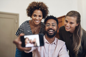 Diverse, fun and happy business people taking a selfie on a phone in an office together. Smiling group of colleagues and friends bonding, laughing and enjoying their positive, healthy friendship