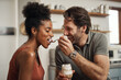 © Allistair/peopleimages.com - Romantic, happy and interracial couple eating a healthy yogurt together in a cute, sweet and fun kitchen romance. Loving, in love and excited husband feeding his beautiful afro wife delicious dessert