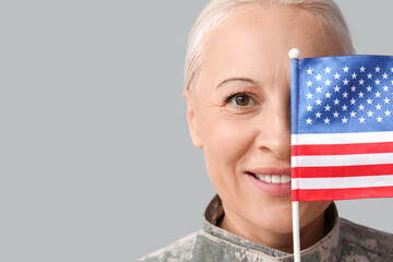 Wall Mural - Mature female soldier with USA flag on grey background, closeup