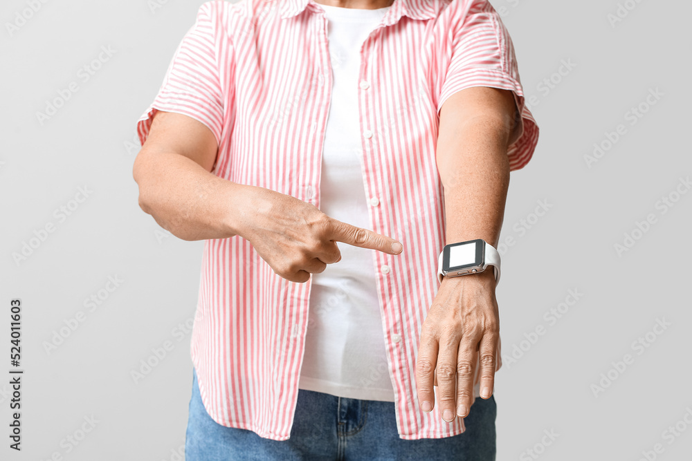 Mature woman pointing at smartwatch for navigation on light background, closeup