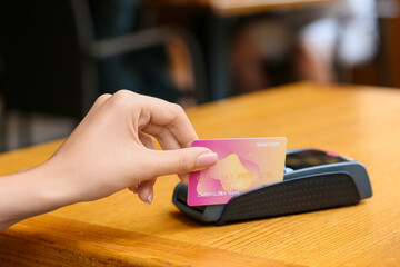 Wall Mural - Woman paying with credit card via payment terminal at table in cafe, closeup