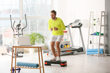 Poster - Sporty young man using laptop for online training in gym