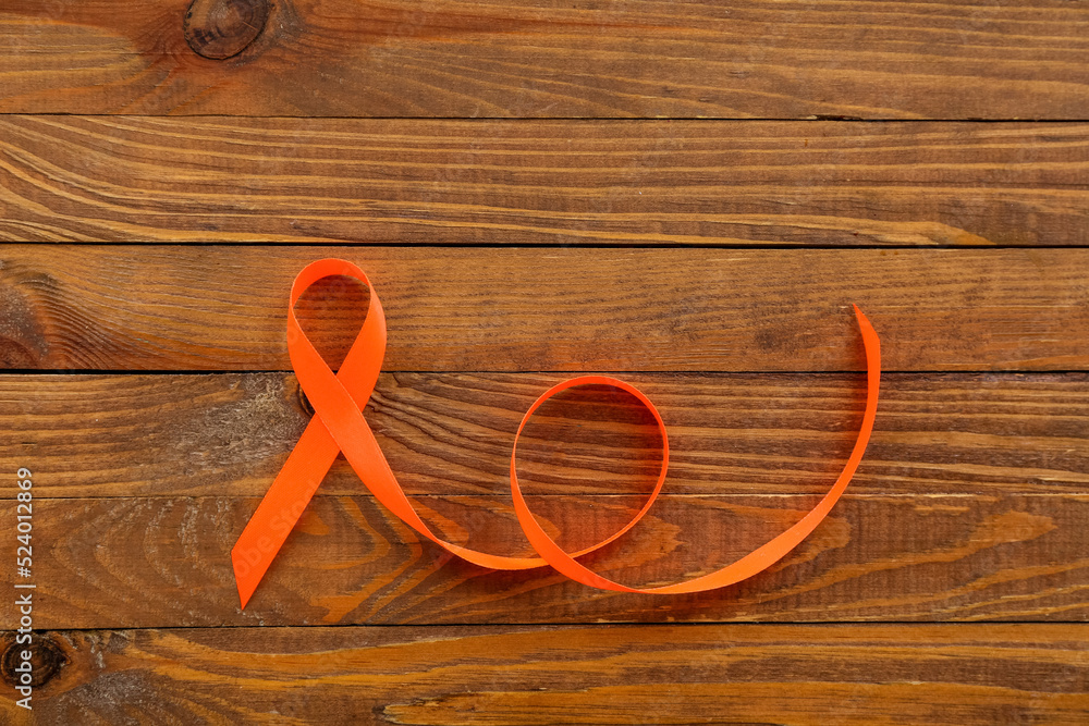 Orange awareness ribbon on wooden background. Kidney cancer concept