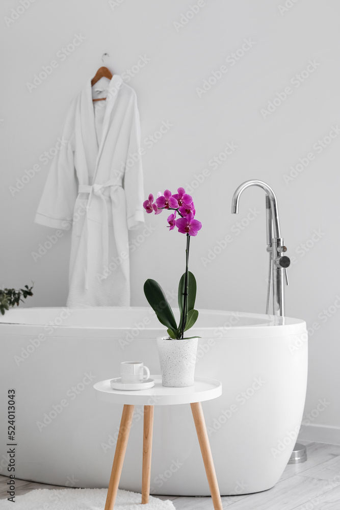 Orchid flower and cup on table near bathtub