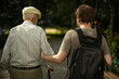 © Олег Копьёв - Son leads his father down street. Grandson holds his grandfather's arm. Man helps pensioner.