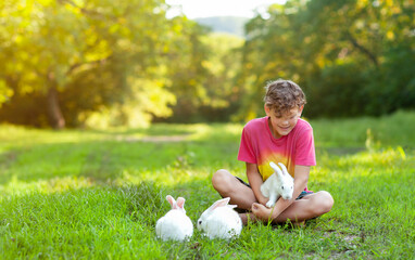 A boy is playing with white rabbits in a green clearing