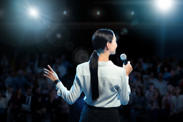 Motivational speaker with microphone performing on stage, back view
