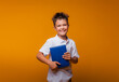 © inna717 - a schoolboy boy holds a blue book on a yellow background. back to school.