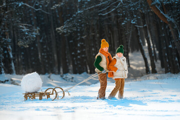 Family entertainment in winter with snow. Two happy smiling children playing pulling a sled with a snow globe. Children have fun with snowballs.