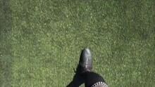 POV Shot Looking Down At A Football Player's Boots As He Walks Across An Artificial Soccer Pitch On A Sunny Day