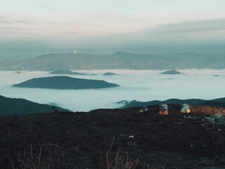 Poster - Breathtaking view of clouds covering the hills with colorful tents in the foreground