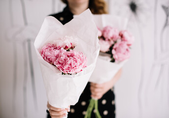 Wall Mural - Very nice young woman's hand holding big and beautiful bouquet of fresh white and pink peony flowers, wrapped i pink paper on the pink background, bouquet close up