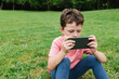 © ADDICTIVE STOCK - Boy using smartphone on park lawn