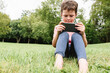 © ADDICTIVE STOCK - Happy boy using smartphone on park lawn