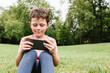 © ADDICTIVE STOCK - Happy boy using smartphone on park lawn