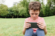 © ADDICTIVE STOCK - Boy using smartphone on park lawn