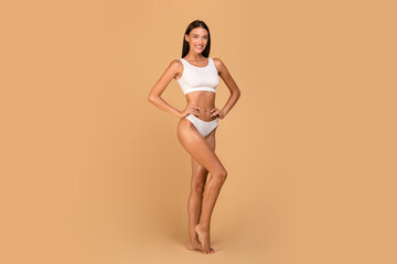 Wall Mural - Young slender caucasian lady posing in white underwear over beige studio background, full length shot, copy space