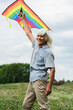 © LIGHTFIELD STUDIOS - happy senior man in casual clothes holding kite and standing on green hill.