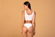 Back view of slim lady in white underwear demonstrating her perfect body, posing against beige studio background