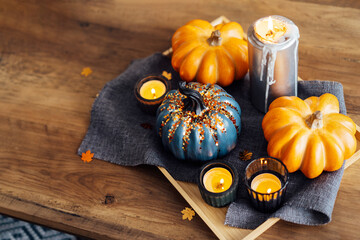 Autumn, fall cozy mood composition for hygge home decor. Decorative orange and gray pumpkins and burning candles on the tray with gray napkin on the wooden coffee table. Selective focus