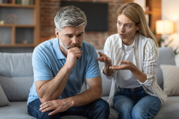 Wall Mural - Sad upset adult caucasian wife yelling at husband, gesticulates in living room interior, close up