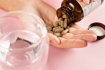 Bottle of weight loss pills and glass of water on pink background. Proper nutrition concept. Holding pills for diet in hand and ready to drink water. Diet with biologically active supplement.